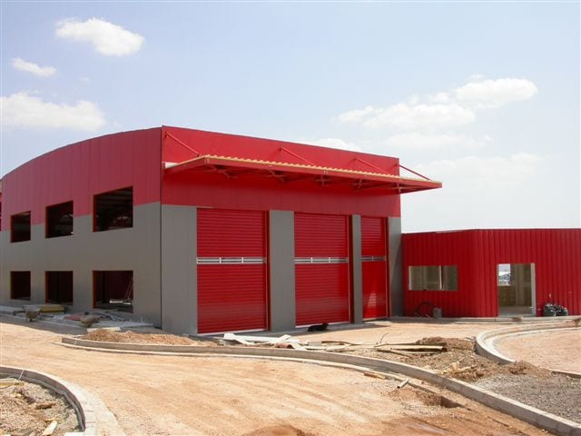 Front facade of the vehicle inspection center in Aspropyrgos with red roller doors and entrance canopy