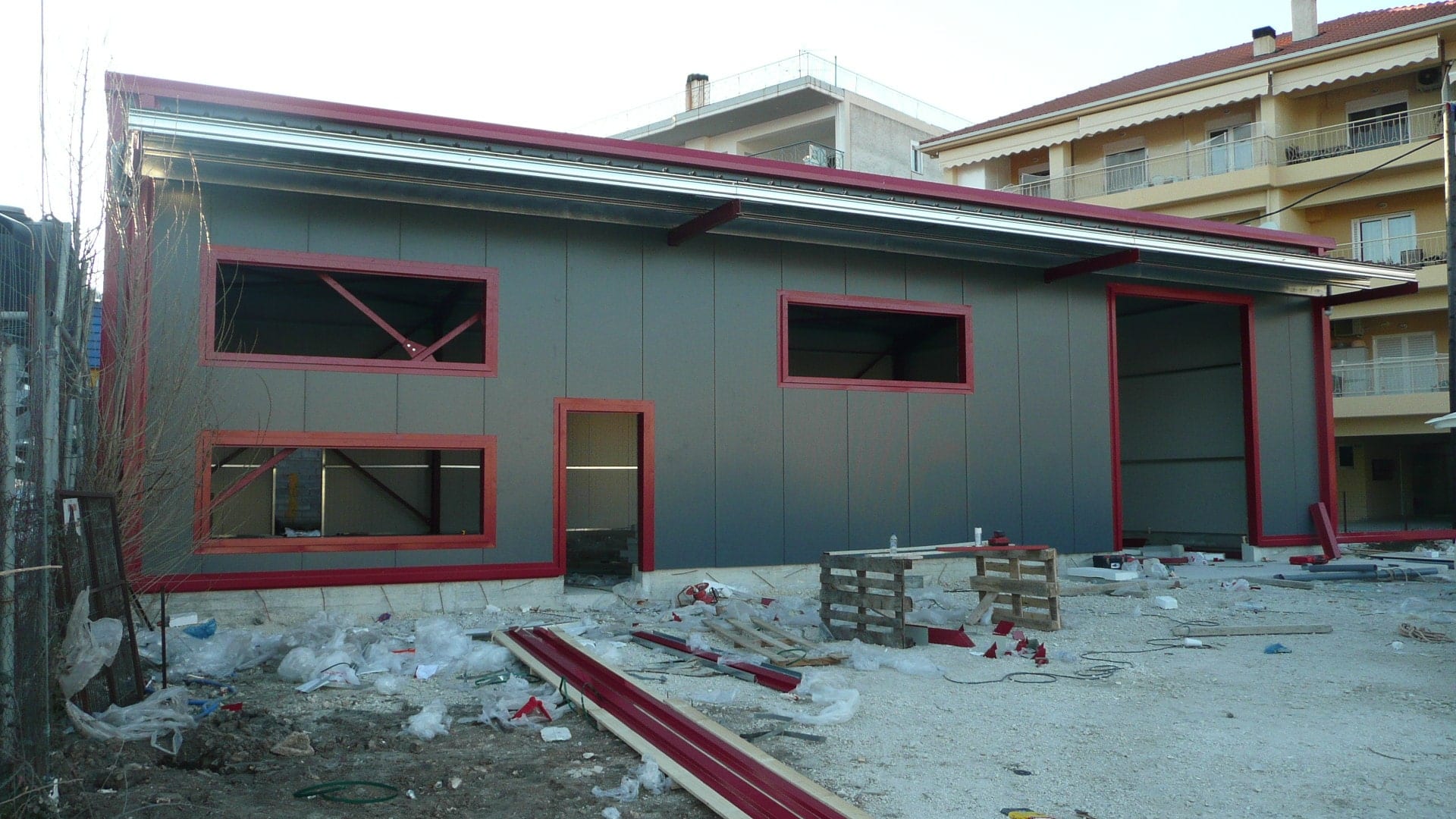 Elevation with gray insulated panels and red opening frames on the olive oil warehouse in Ioannina