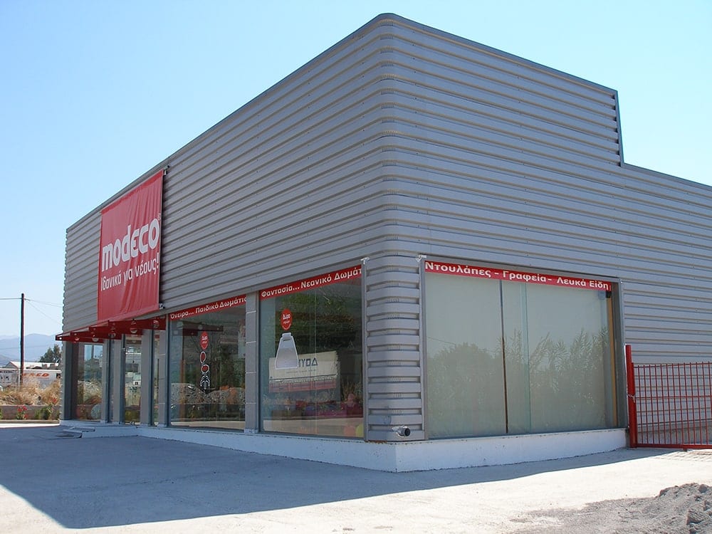Final view of the Modeco showroom in Asprochoma, Messinia, with horizontal metal sheet and shop windows