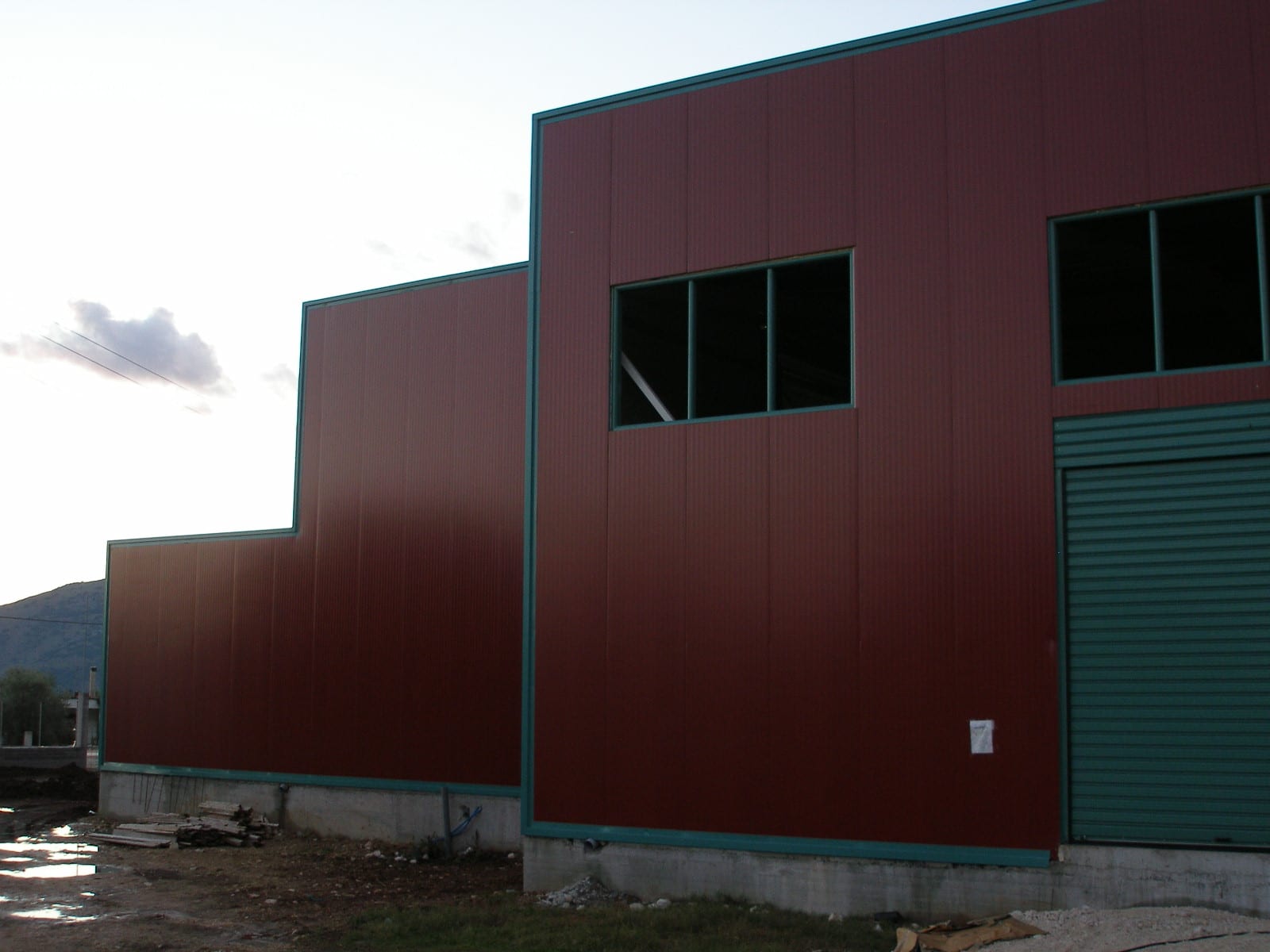 Wall cladding with red insulated panels and an industrial roller door at the distillery in Paramythia